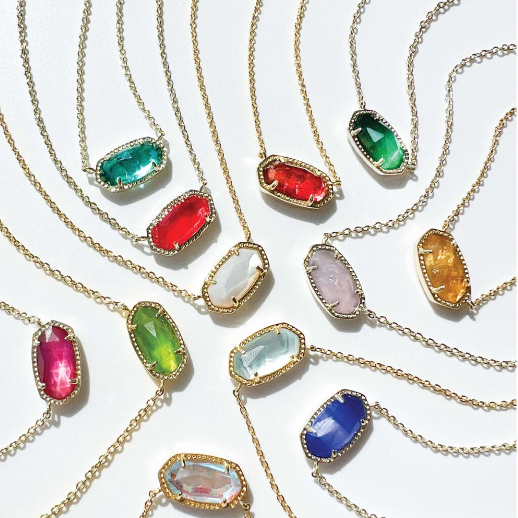 Eleven gold necklaces with faceted oval-shaped pendants in various colors, arranged in a circular pattern on a white surface.